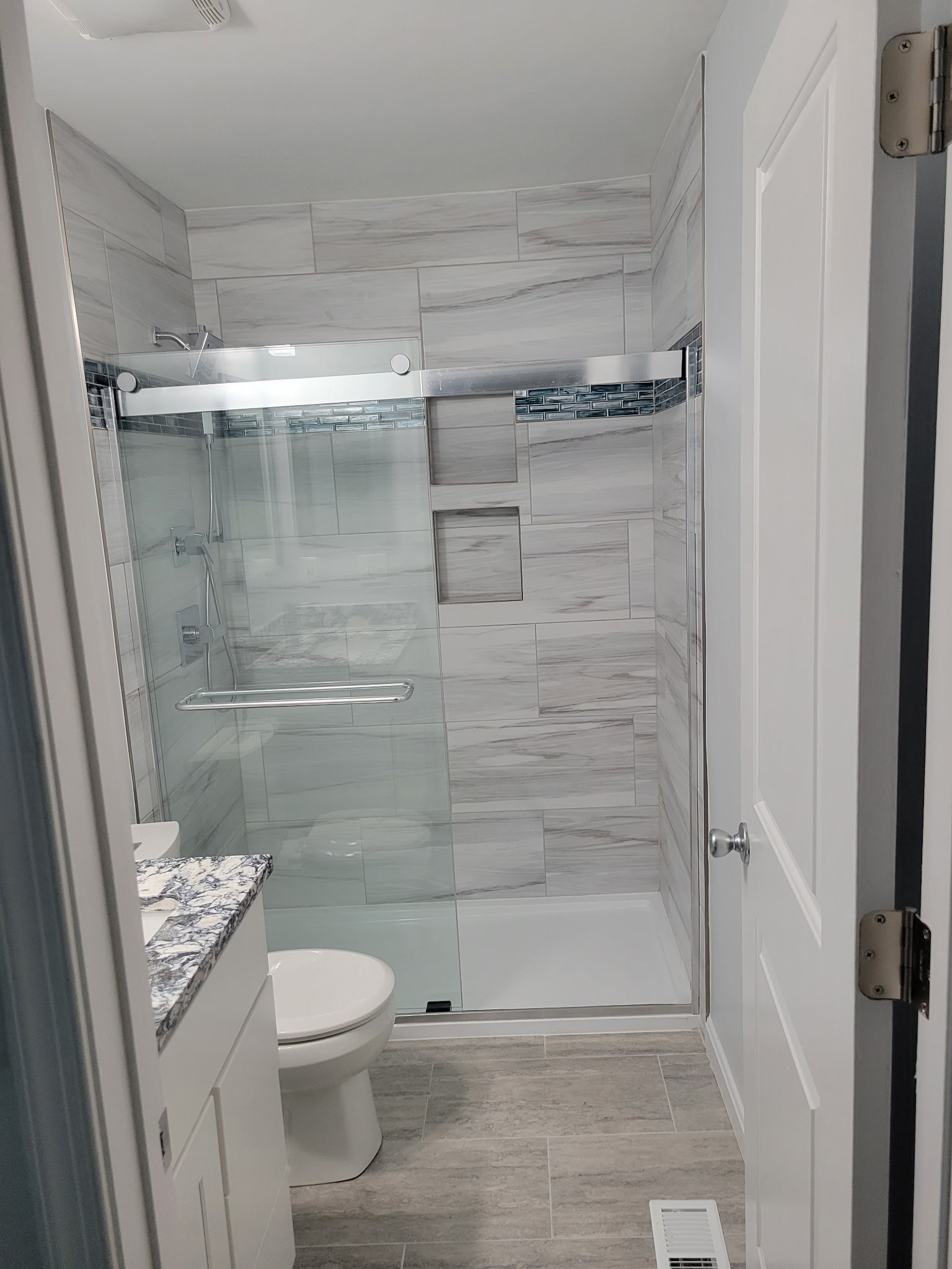 Finished gray tile walk-in shower with a glass enclosure and built-in niche